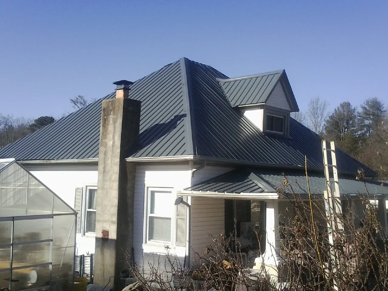 Dark blue standing seam metal roof on a white farmhouse with dormer — Slate & Tile Roof Repair by Roofing Brothers in Henderson