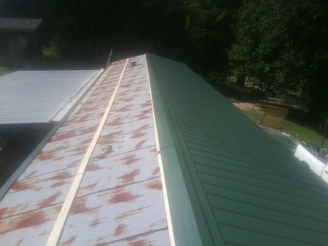 Old rusted panels beside newly installed green metal roofing in Henderson